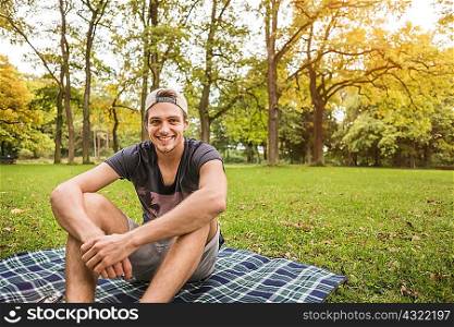 Portrait of young man sitting on picnic blanket in park