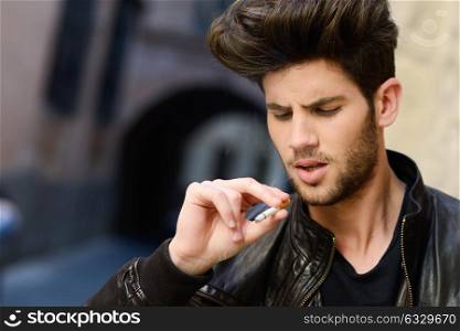 Portrait of young man smoking a cigarette in urban background