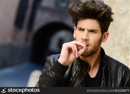 Portrait of young man smoking a cigarette in urban background