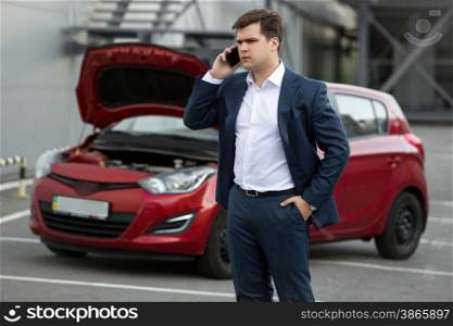 Portrait of young man standing to broken car and calling repair service