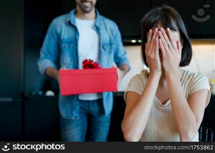 Portrait of young man surprising his girlfriend with a gift box. Celebration and valentine&rsquo;s day concept.