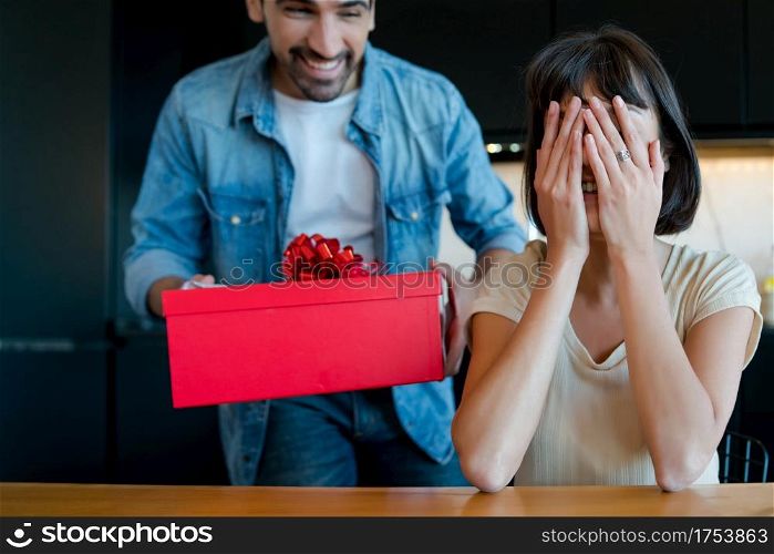 Portrait of young man surprising his girlfriend with a gift box. Celebration and valentine&rsquo;s day concept.