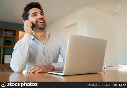 Portrait of young man talking on his mobile phone and working from home with laptop. Home office concept. New normal lifestyle.