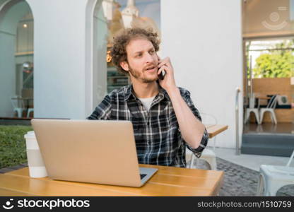 Portrait of young man talking on the phone while sitting in a coffee shop. Communication concept.