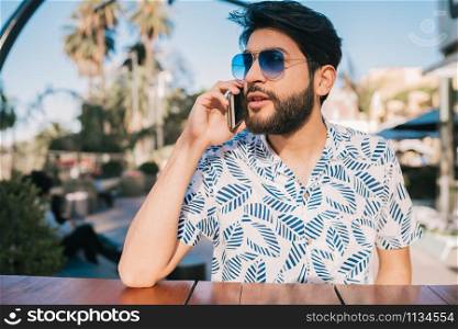 Portrait of young man talking on the phone while sitting in a coffee shop outdoors. Communication concept.