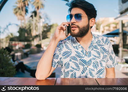 Portrait of young man talking on the phone while sitting in a coffee shop outdoors. Communication concept.