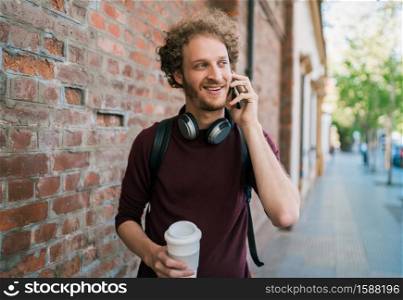 Portrait of young man talking on the phone while walking outdoors in the street. Communication and urban concept.