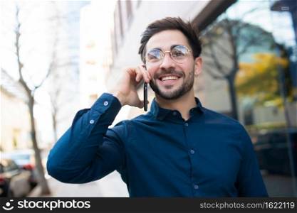 Portrait of young man talking on the phone while walking outdoors on the street. Urban concept.