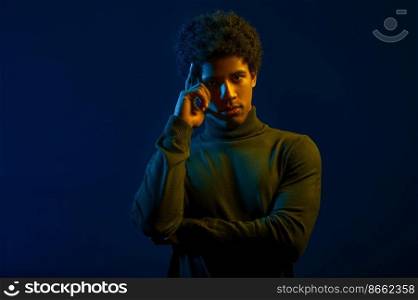 Portrait of young man thinking holding finger to temple over dark studio background. Young man holding finger to temple portrait