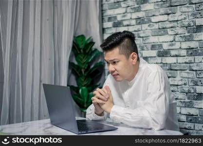 Portrait of young man thinking while serious working at home with laptop on desk