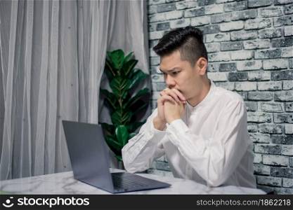 Portrait of young man thinking while serious working at home with laptop on desk