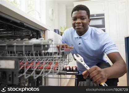 Portrait Of Young Man Training As Plumber Fixing Domestic Dishwasher In Kitchen