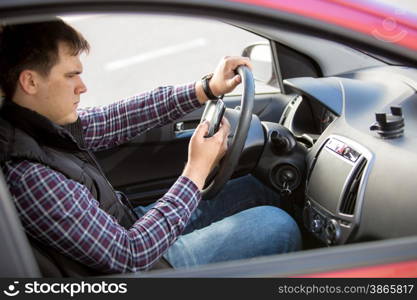 Portrait of young man typing message while driving a car