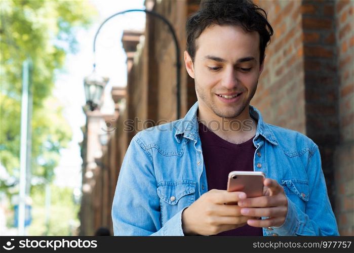 Portrait of young man typing on his phone in the street. Outdoors.