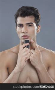 Portrait of young man using electric shaver