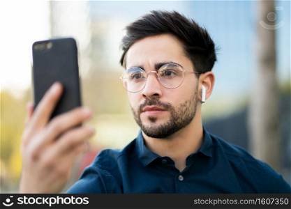 Portrait of young man using face id for unlock mobile phone while standing outdoors. Technology concept.. Young man using face id for unlock mobile phone outdoors.
