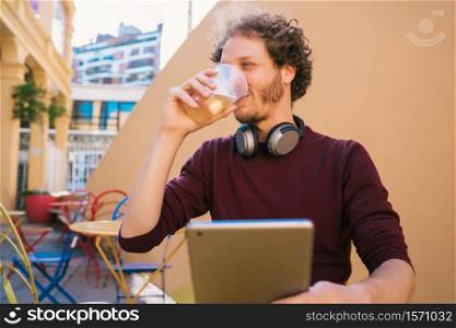 Portrait of young man using his digital tablet while drinking beer. Technology and lifestyle concept