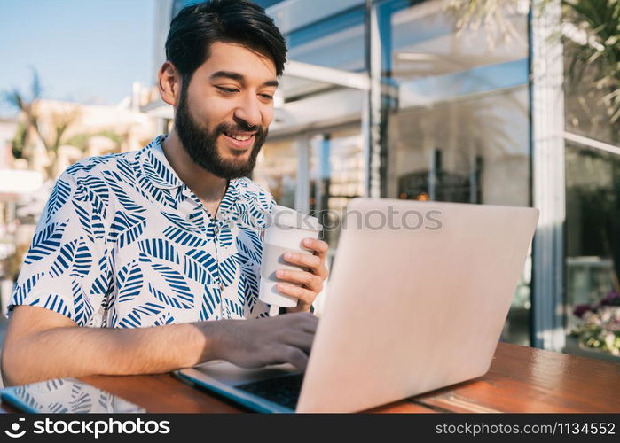 Portrait of young man using his laptop while sitting in a coffee shop and drinking a cup of coffee. Technology and business concept.