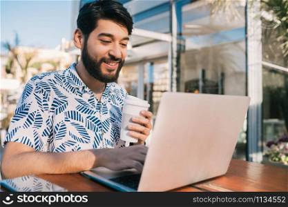 Portrait of young man using his laptop while sitting in a coffee shop and drinking a cup of coffee. Technology and business concept.