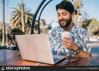 Portrait of young man using his laptop while sitting in a coffee shop and drinking a cup of coffee. Technology and business concept.