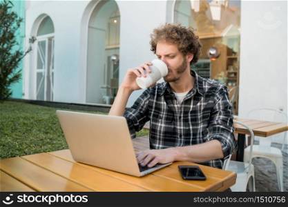 Portrait of young man using his laptop while sitting in a coffee shop. Technology and lifestyle concept.