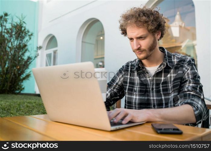 Portrait of young man using his laptop while sitting in a coffee shop. Technology and lifestyle concept.