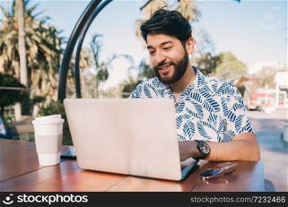 Portrait of young man using his laptop while sitting in a coffee shop. Technology and business concept.