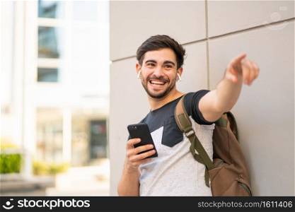 Portrait of young man using his mobile phone and pointing at something outdoors. Urban concept.