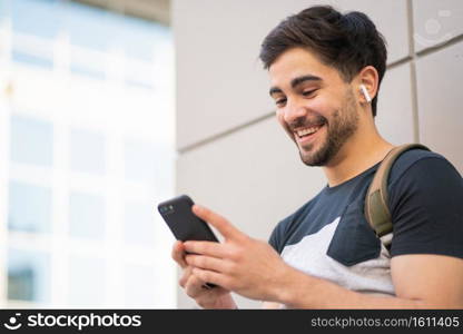 Portrait of young man using his mobile phone while standing outdoors on the street. Urban concept.