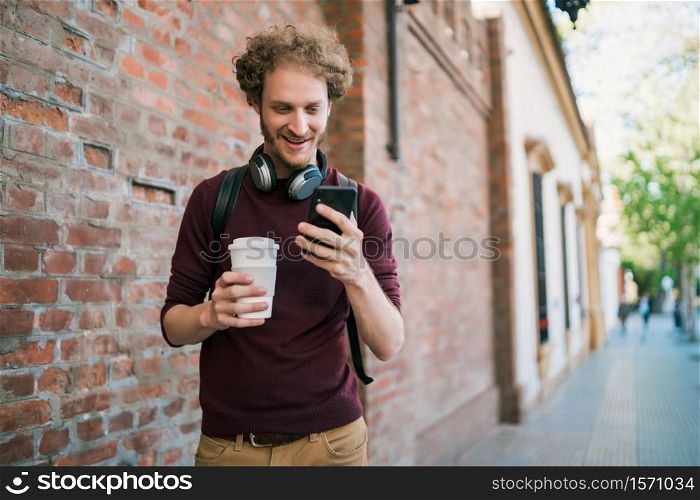 Portrait of young man using his mobile phone while walking outdoors in the street. Communication and urban concept.