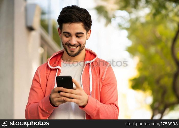 Portrait of young man using his mobile phone while walking outdoors on the street. Urban concept.