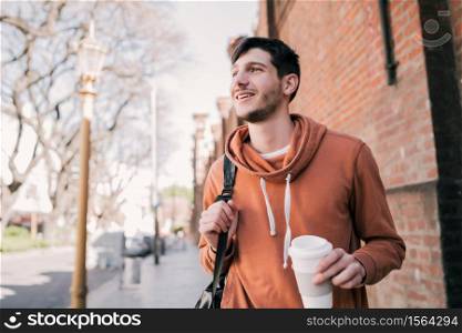 Portrait of young man walking and holding a cup of coffee outdoors on the street. Urban concept.