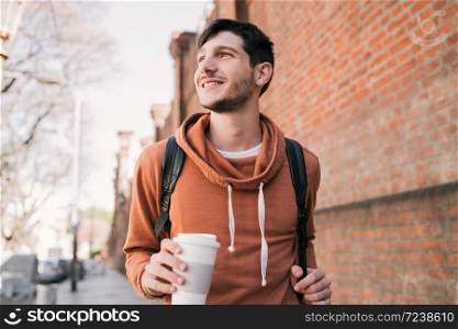 Portrait of young man walking and holding a cup of coffee outdoors on the street. Urban concept.