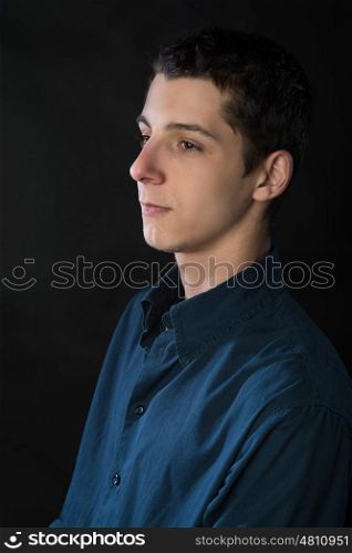 portrait of young man wearing blue shirt against black background