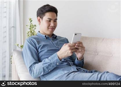 Portrait of young man wearing blue shirt is looking with smartphone and sitting at his sofa in the office.
