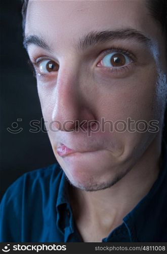 portrait of young man wearing blue shirt making silly faces against black background