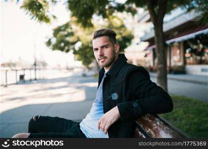 Portrait of young man wearing winter clothes and sitting on a bench in the street. Urban concept.