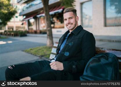 Portrait of young man wearing winter clothes and sitting on a bench in the street. Urban concept.