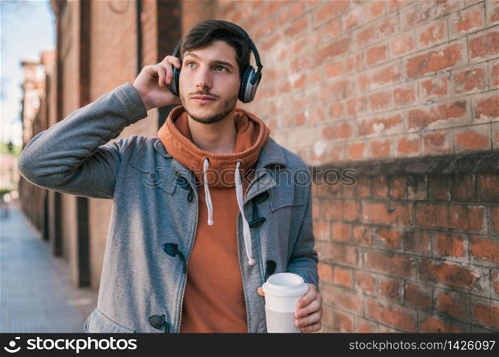 Portrait of young man with earphones and a cup of coffee against brick wall. Outdoors. Urban concept.