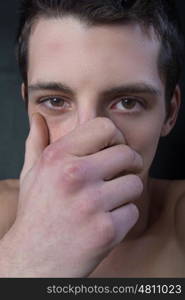 portrait of young man with hand on mouth on black background