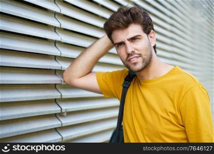 Portrait of young man with modern haircut looking away in urban background. Young man with modern haircut in urban background