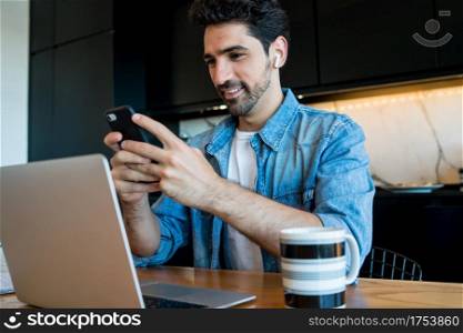 Portrait of young man working with a laptop and using his mobile phone from home. Home office concept. New normal lifestyle.