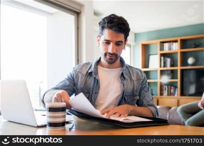 Portrait of young man working with a laptop from home while woman talking on phone at background. Home office concept. New normal lifestyle.