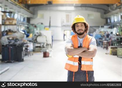 Portrait of young manual worker standing arms crossed in factory