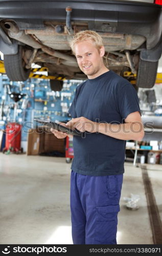 Portrait of young mechanic standing and using digital tablet in his auto repair shop