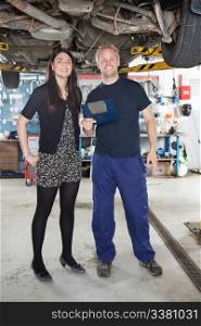 Portrait of young mechanic standing with female customer in auto repair shop