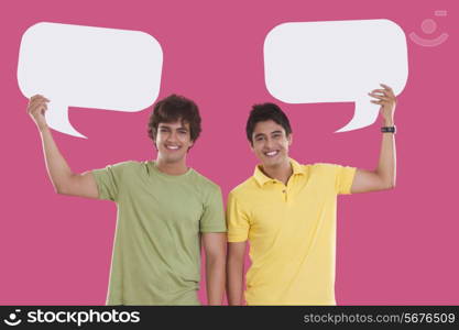 Portrait of young men holding speech bubbles over pink background