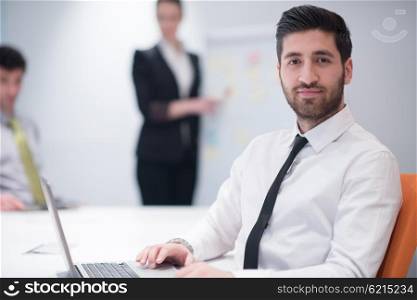 portrait of young modern arab business man with beard at office meeting room, group of business people on brainstorming and making plans and projects on white flip board in background