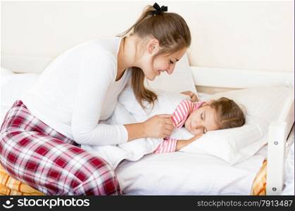 Portrait of young mother covering little sleeping girl with blanket