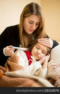 Portrait of young mother embracing sick daughter and checking thermometer